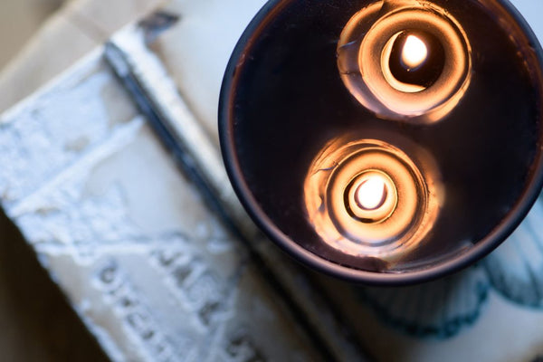 flat lay image looking over the top of a black two wick candle that is lit with the wax pooling