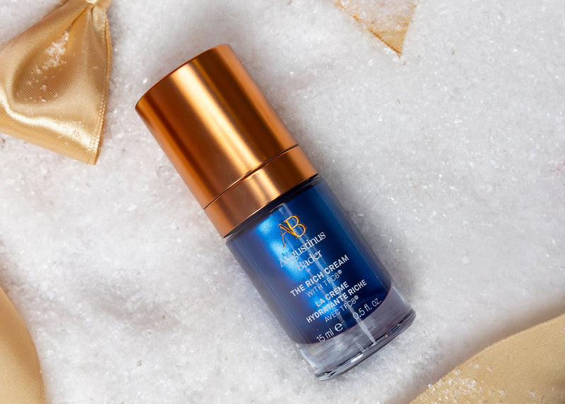 Blue skincare serum bottle with gold cap on a white background with gold ribbons