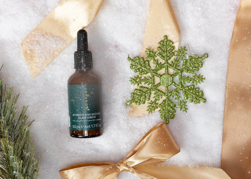 Skincare serum bottle with gold ribbons and a green snowflake on a white background