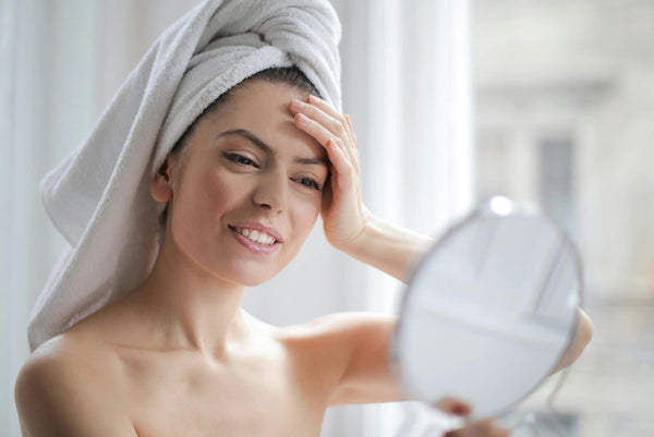 woman wearing hair towel looking into a mirror and smiling at her reflection