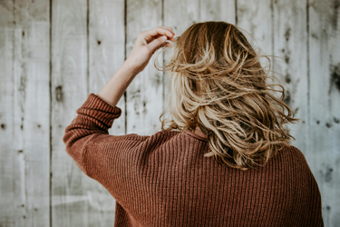 a woman wearing a brown cardi with short blonde hair with her back to the camera
