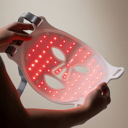 LED face mask with red lights held by a person against a neutral background