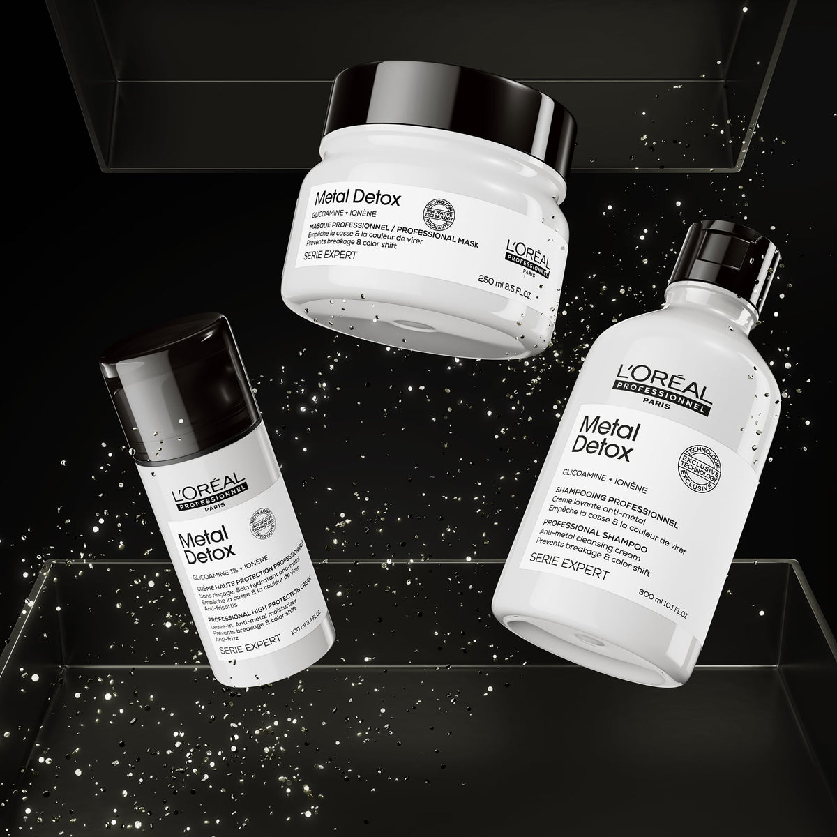 Three L'Oréal Professionnel Paris Metal Detox haircare products floating on a black background with spark effects: a white jar with a black lid, a white bottle with a black cap, and a white tube with a black cap. The products are labeled 'Metal Detox' and 'Série Expert'.