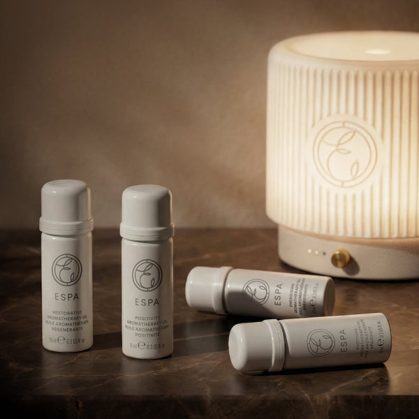 ESPÓA skincare products on a wooden surface with a lit diffuser in the background.
