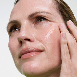 Close-up of a woman's face with a hand touching her cheek, against a white background