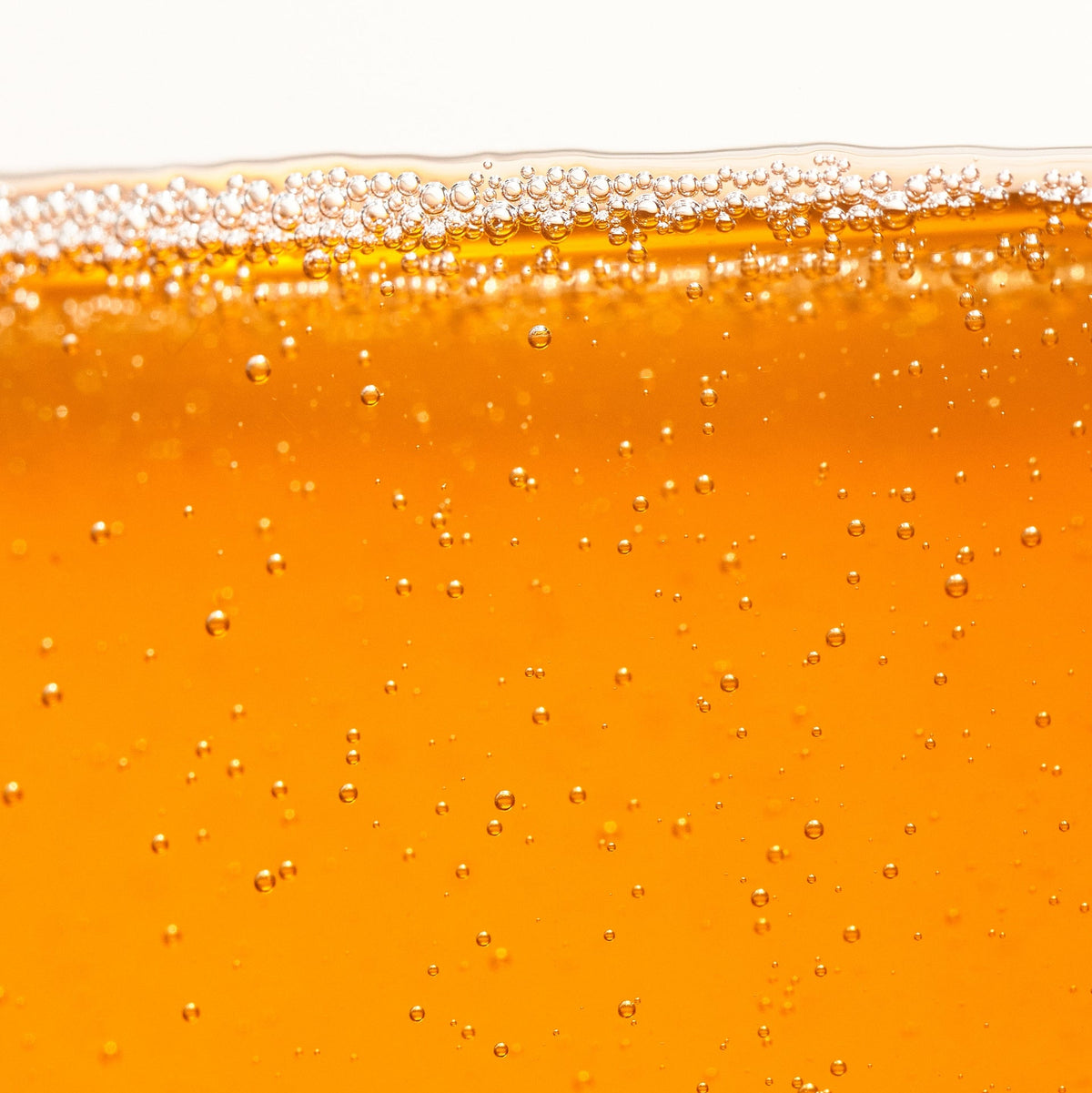 Close-up of a glass filled with orange liquid, likely beer, with bubbles on a white background.