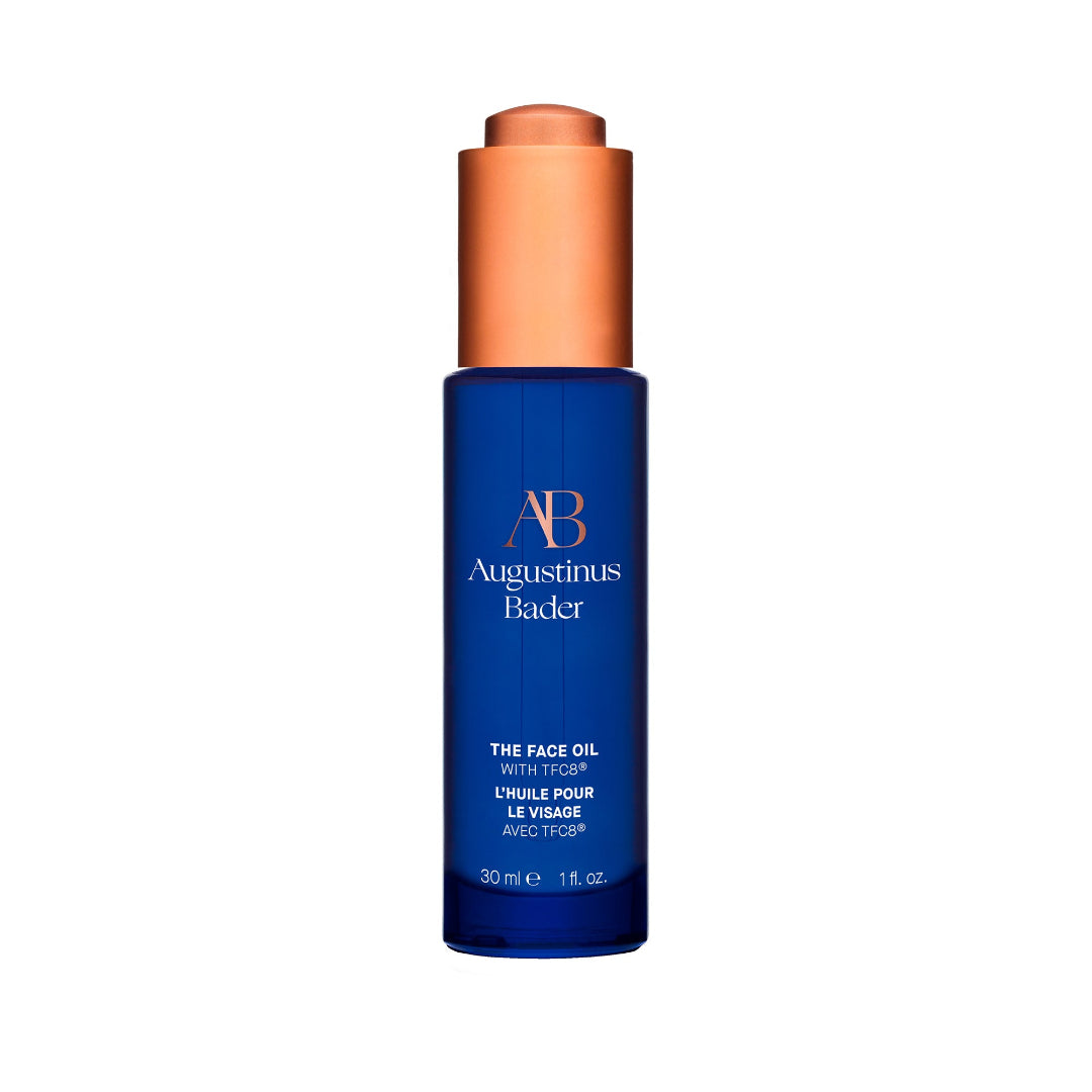 Blue bottle of Augustinus Bader face oil with a copper cap on a white background