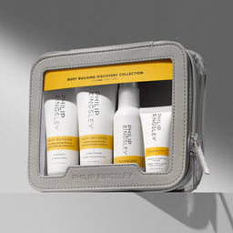 Philip Kingsley Body Building Discovery Collection travel set in a gray zippered pouch, containing four white and yellow shampoo, conditioner, body butter, and treatment bottles.