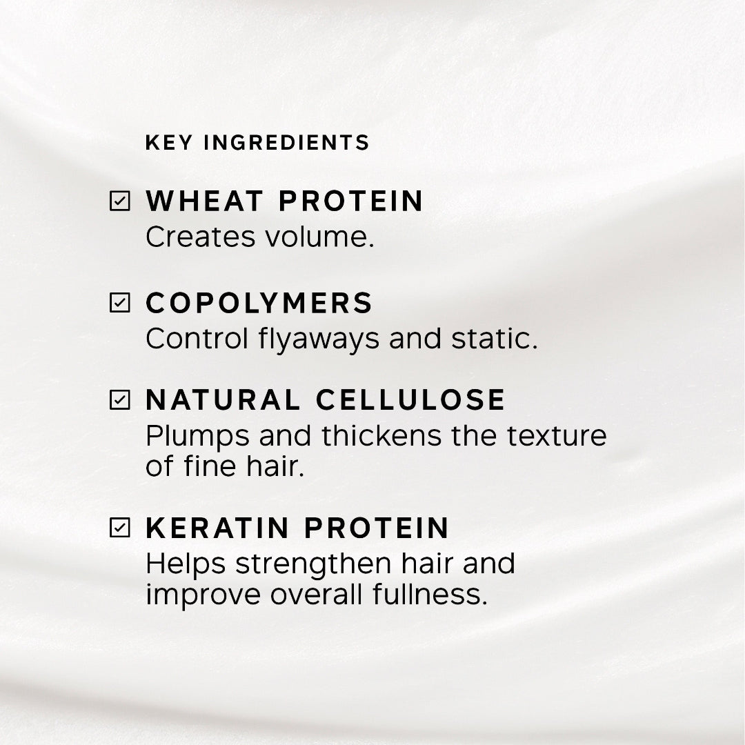 A close-up of a white or very light beige fabric background with black text listing key ingredients: wheat protein, copolymers, natural cellulose, and keratin protein, each with a checkmark.