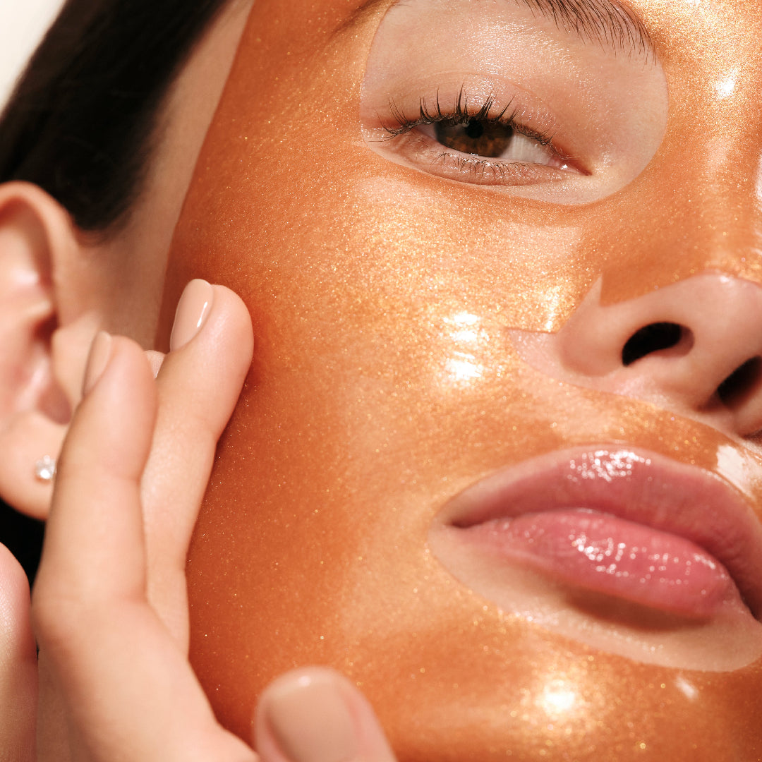 Close-up of a person's face with a bronze-colored mask on, touching their cheek.