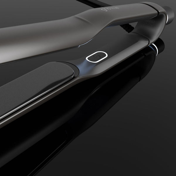 A sleek black and dark gray hair straightener shown at an angle on a glossy black reflective surface.