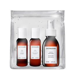 A Sachajuan hair care set in a clear resealable pouch, containing three amber bottles with white caps: conditioner, leave-in conditioner, and moisturizing hair primer, on a white background.