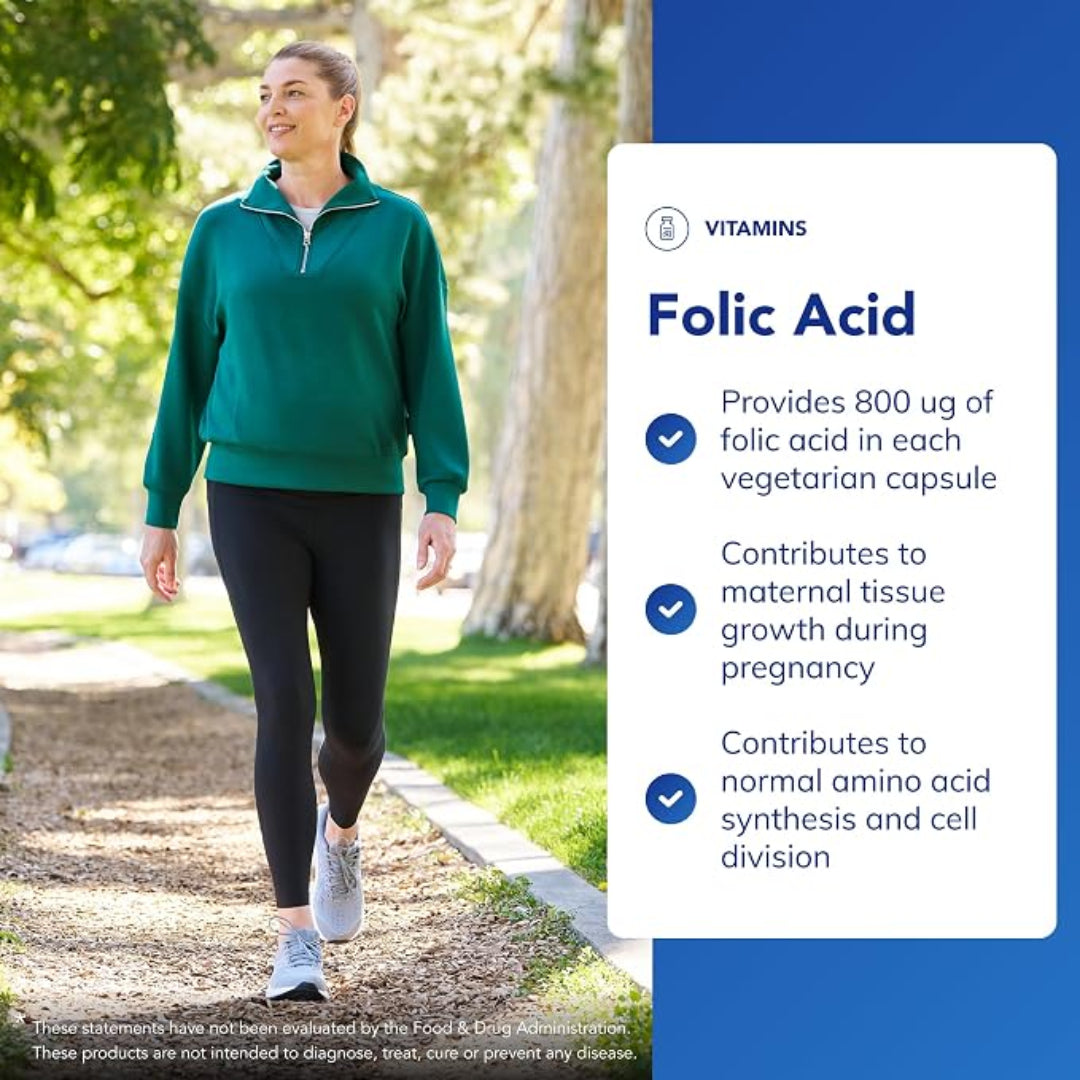 A woman in a green quarter-zip pullover and black leggings walks on a park path next to a large informational graphic about folic acid vitamins.