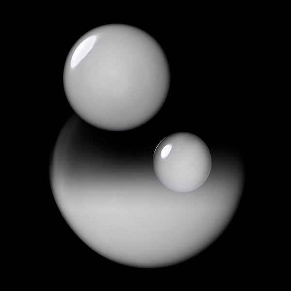 Two glossy white spherical objects floating against a solid black background, with soft reflections below them.