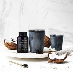 Activated charcoal powder from Kiki Health with two glasses of a dark beverage on a marble surface.