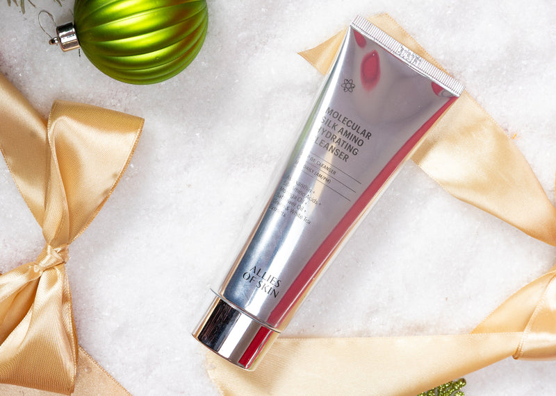 Skincare tube with gold ribbon and green ornament on a snowy background