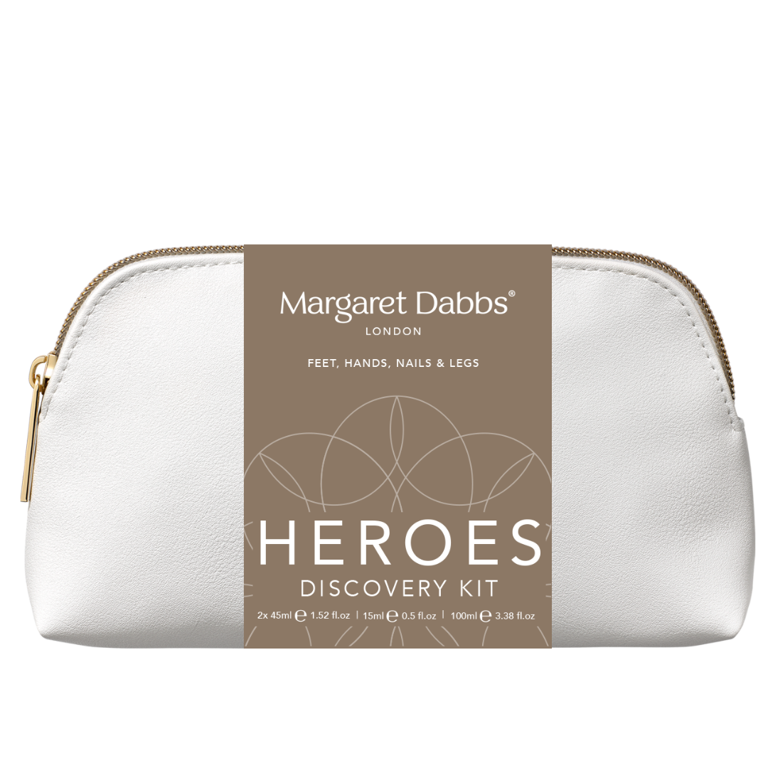 A white pebbled leather cosmetic pouch with a gold zipper, featuring a brown paper label that reads 'Margaret Dabbs London Heroes Discovery Kit'.