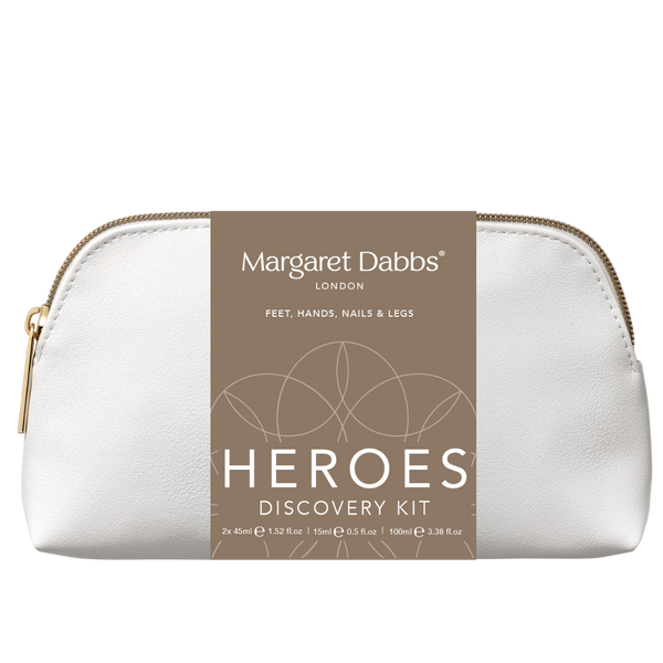 A white pebbled leather cosmetic pouch with a gold zipper, featuring a brown paper label that reads 'Margaret Dabbs London Heroes Discovery Kit'.