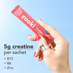 A hand with red nail polish holds a red Zooki Creatine+ sachet against a light blue gradient background, with text on the left stating '5g creatine per sachet + B12 + B6 + Zinc'.