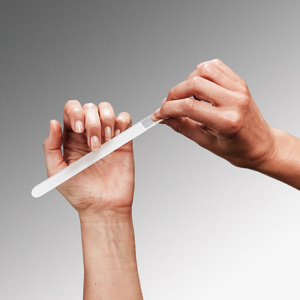 Two hands holding a glass nail file against a gray background