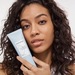 Woman holding a blue hair care product with a neutral background