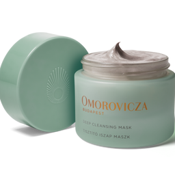 A jar of Omorovicza Deep Cleansing Mask with its lid off, showing the pale mint green jar filled with a thick, light-colored cream, and a matching lid leaning against it on a white background.