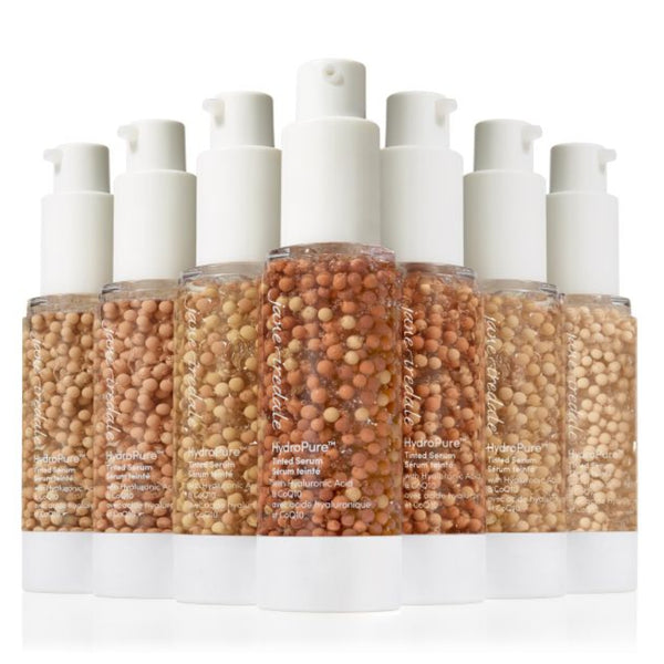 Six clear pump bottles filled with beige and brown cosmetic beads or granules, arranged in a row on a white background.