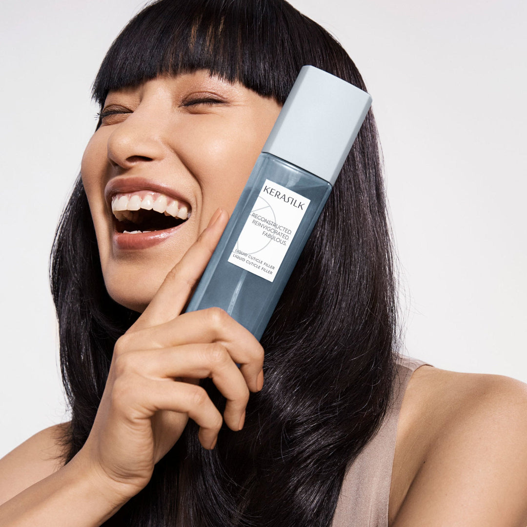 Woman holding a bottle of KeraSilk hair product against a white background