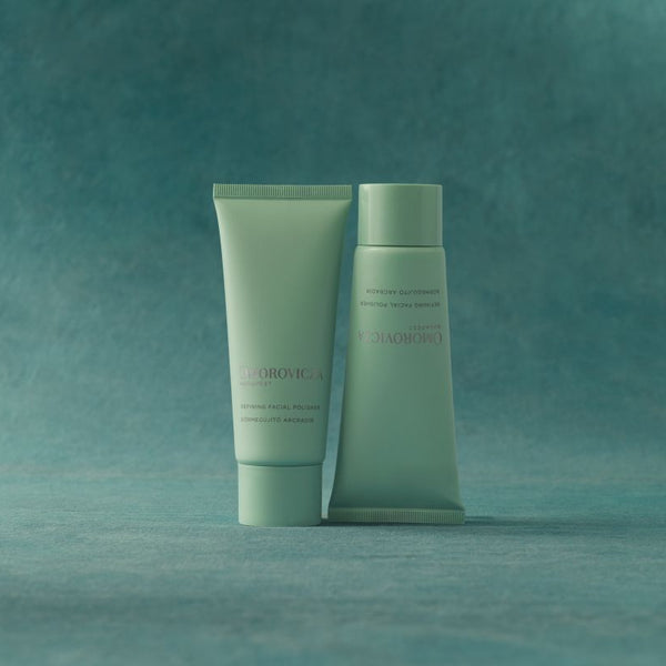 Two pale mint green cosmetic tubes from the brand Scionohydra, standing side-by-side on a textured teal surface against a matching teal background.