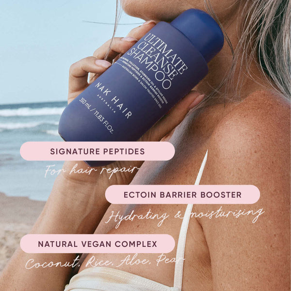 Person holding a bottle of Max Hair shampoo with beach background