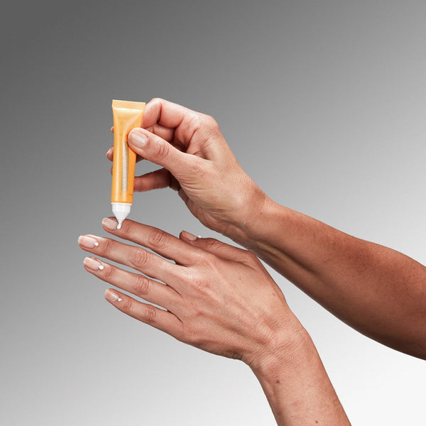 Hand holding an orange tube of cream against a gray background