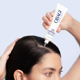 Person applying Obagi product to hair with a blue background