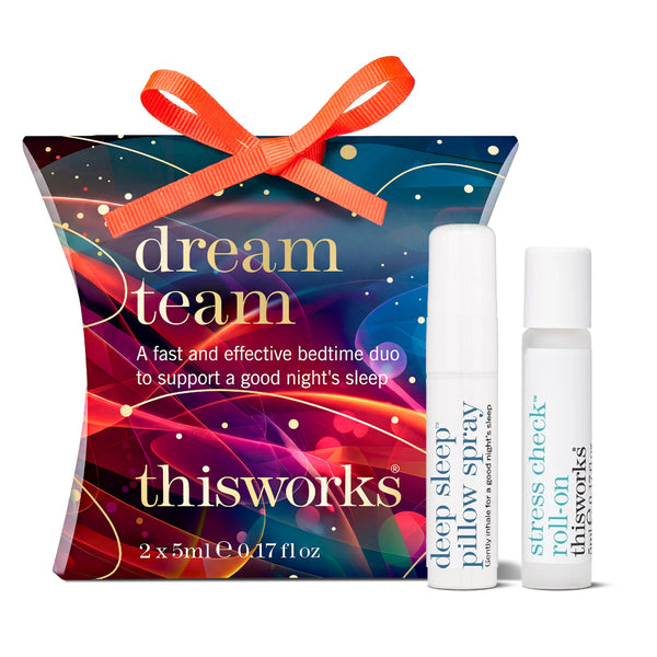 Thisworks Dream Team gift set featuring a colorful gift box with an orange ribbon, alongside two white spray bottles labeled deep sleep pillow spray and stress check roll-on.