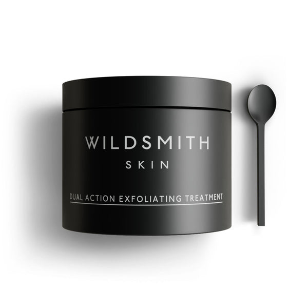 A matte black jar of Wildsmith Skin Dual Action Exfoliating Treatment, shown next to a matching black spoon on a clean white background.