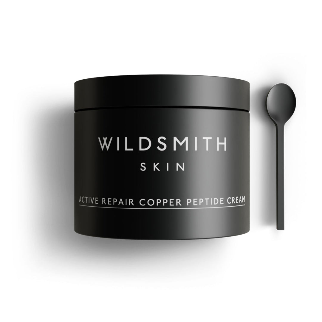A matte black cosmetic jar labeled 'WILDSMITH SKIN' with white text reading 'ACTIVE REPAIR COPPER PEPTIDE CREAM,' shown on a white background with a matching black spoon to the right.