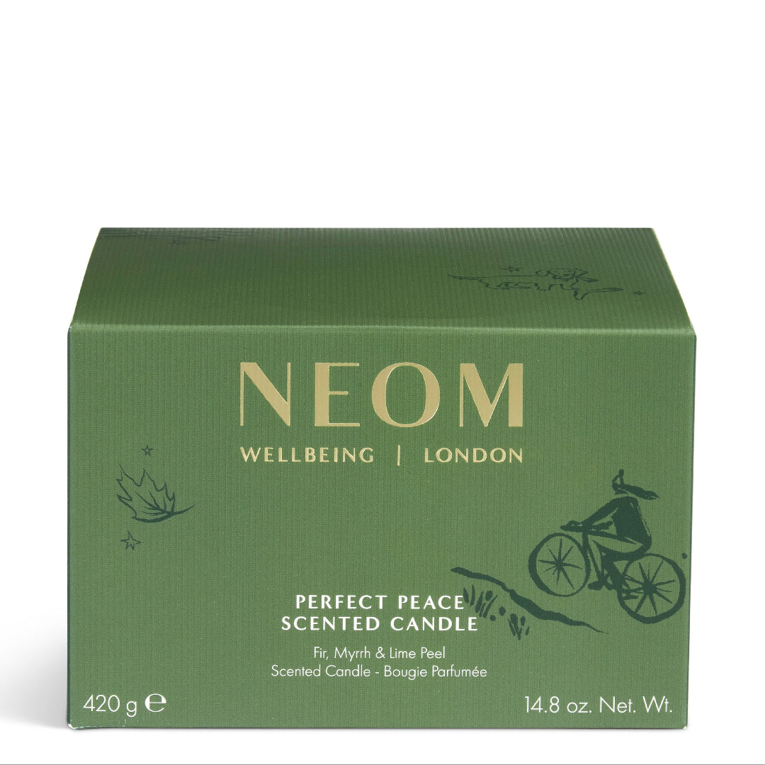 A green rectangular box of NEOM Wellbeing London 'Perfect Peace' scented candle, featuring gold lettering and a black line art illustration of a cyclist, set against a plain white background.