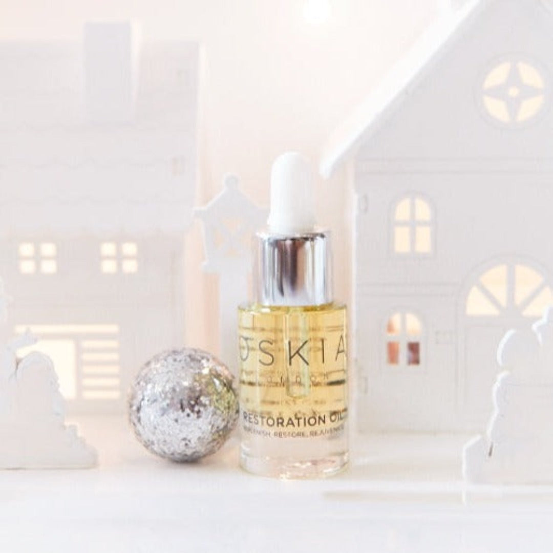 OSKIA Restoration Oil Travel bottle in front of christmas houses