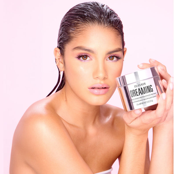 Woman holding a jar of 'Dreaming' skincare product against a pink background
