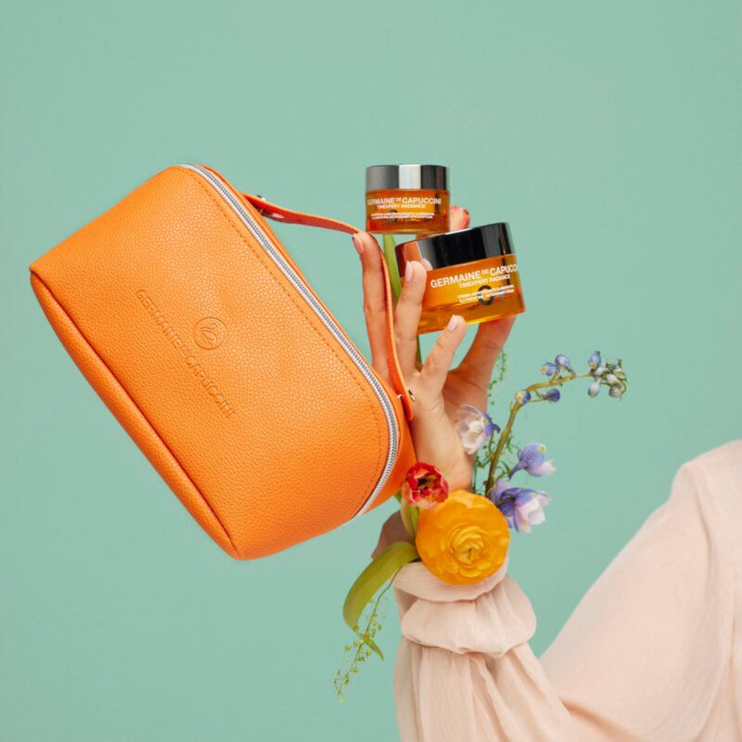 Person holding skincare products and an orange pouch against a light green background