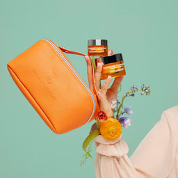 Person holding skincare products and an orange pouch against a light green background