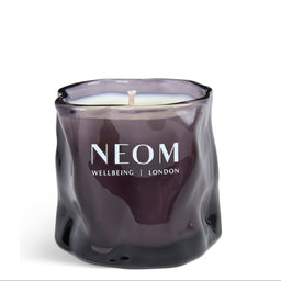A dark purple glass jar candle with a wavy, organic shape and white wax inside, featuring the brand name 'NEOM' printed in white on the front, set against a plain white background.