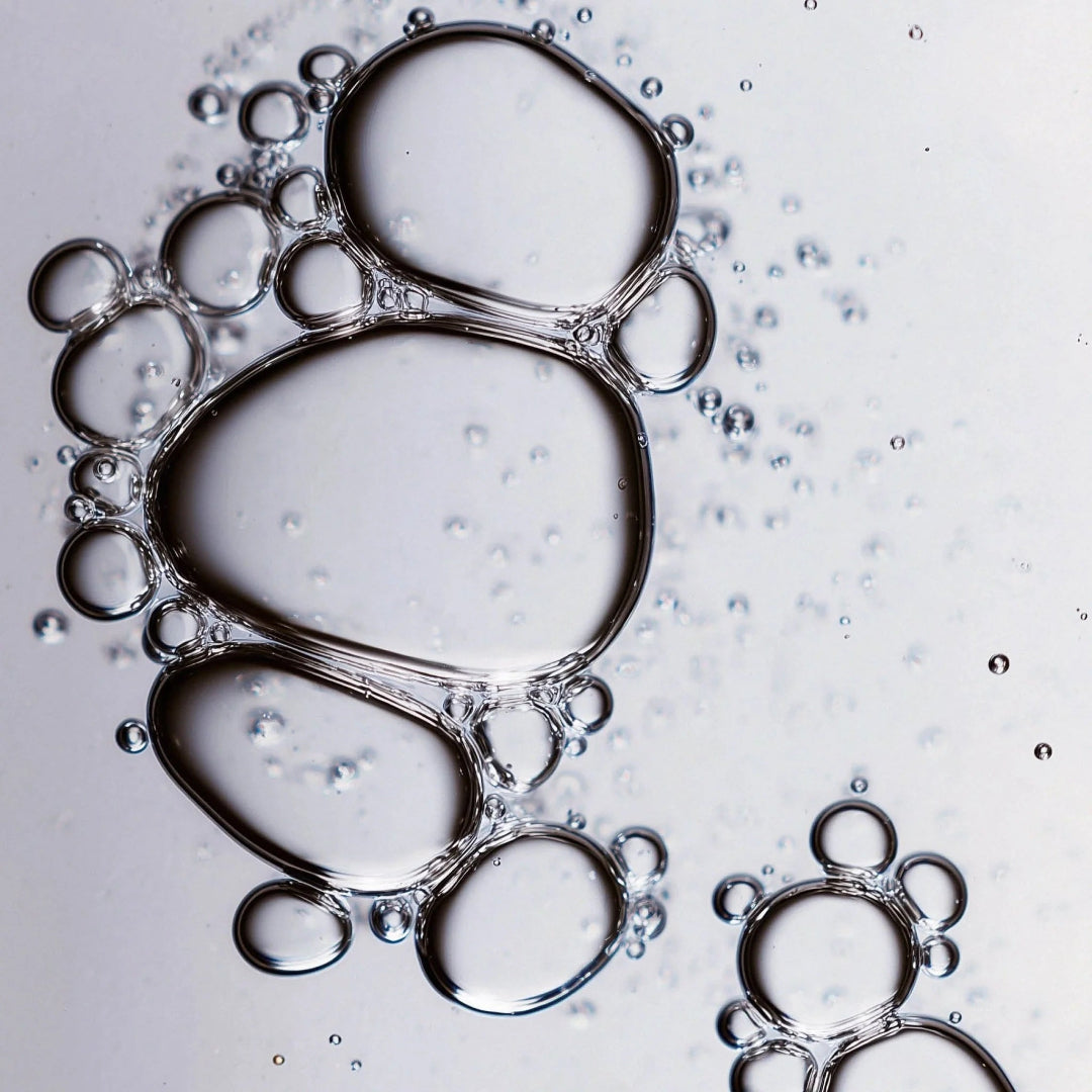 Close-up of clear liquid droplets and transparent bubbles on a light gray background.