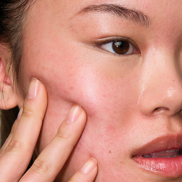 Close-up of a person touching their cheek with their finger, showing skin texture.