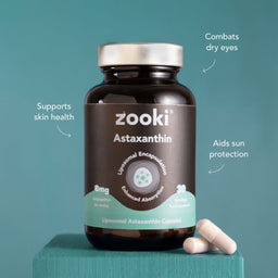 A bottle of Zooki Astaxanthin dietary supplement capsules on a teal background, with three capsules resting beside the bottle and white text callouts describing benefits.