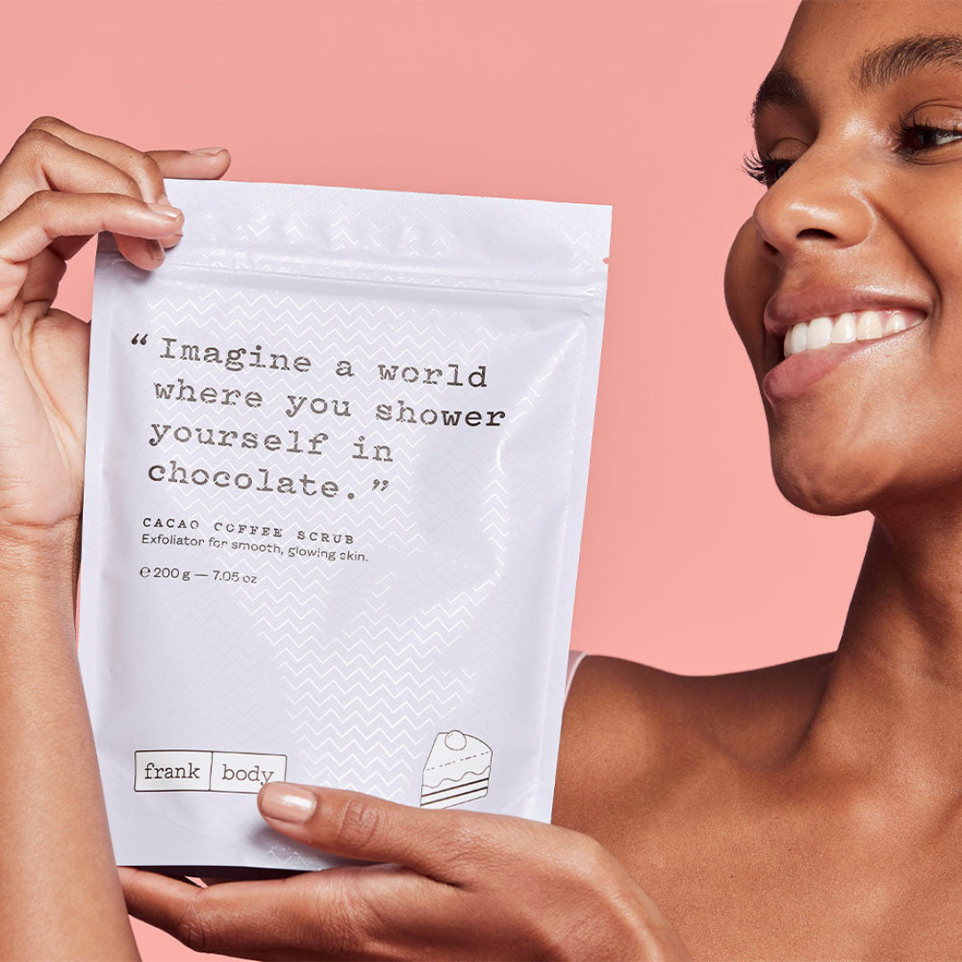Person holding a 'frank body' scrub packet with a pink background