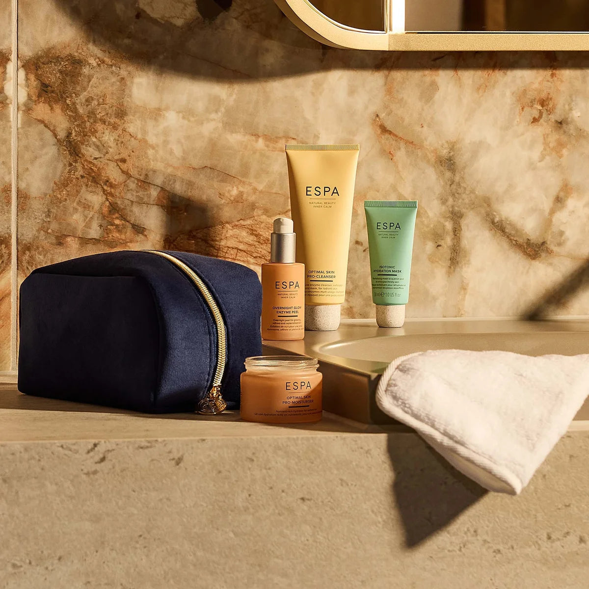 Espa skincare products on a marble countertop with a navy blue pouch.