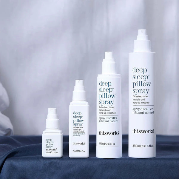 Collection of 'thisworks' deep sleep pillow spray bottles on a bed with a blurred background.