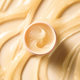 Close-up of a container of light-colored cream or frosting on a swirling patterned background.