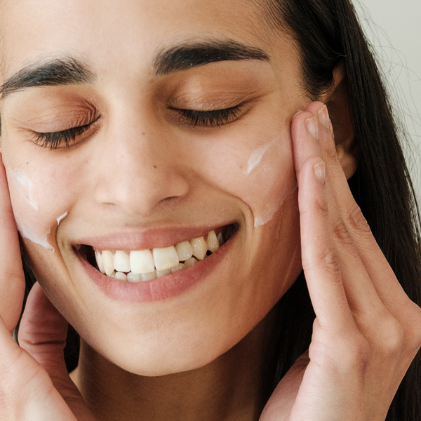 Woman applying cream to her face with a neutral background