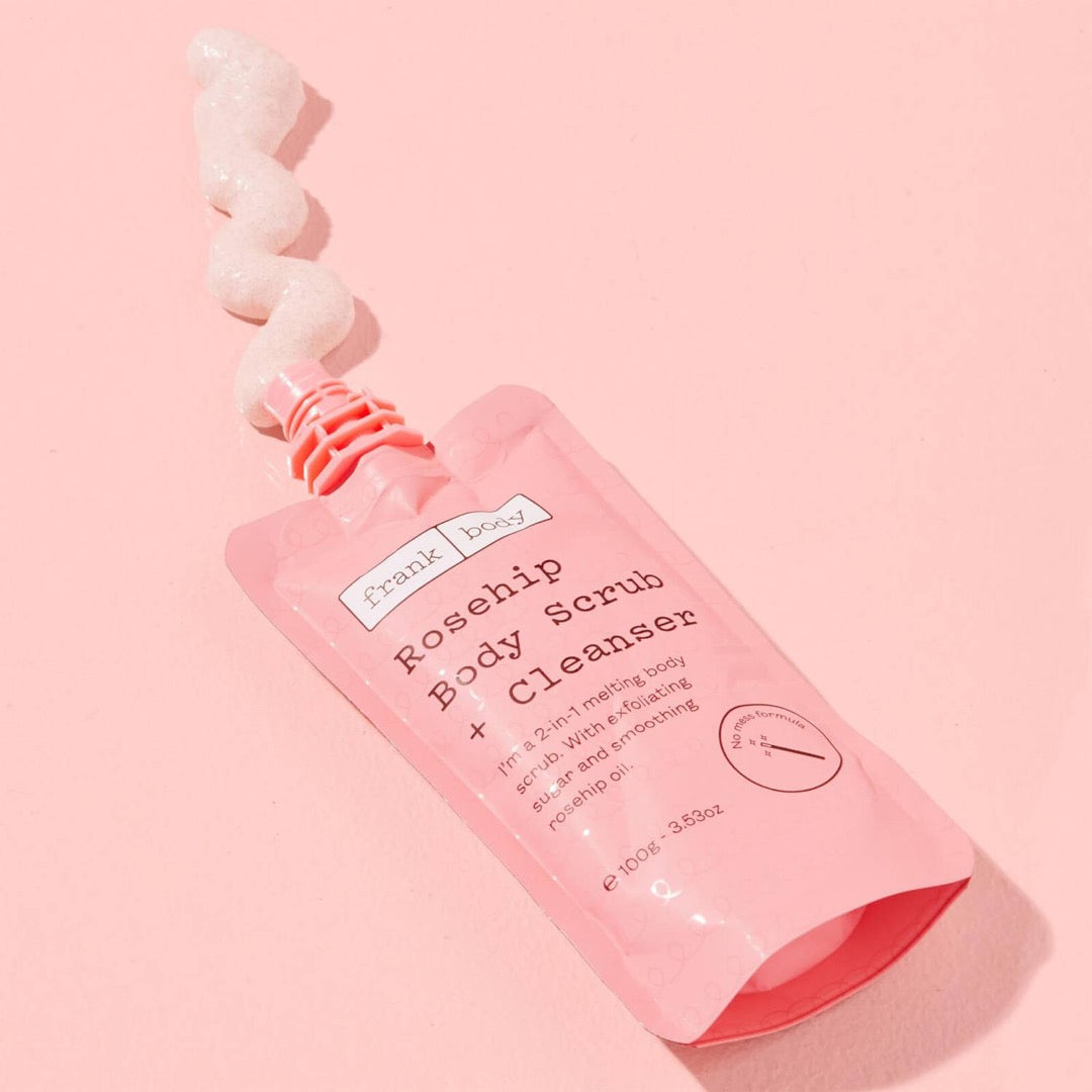 Frank Body Rosehip Body Scrub + Cleanser with its contents poured out onto a pink surface
